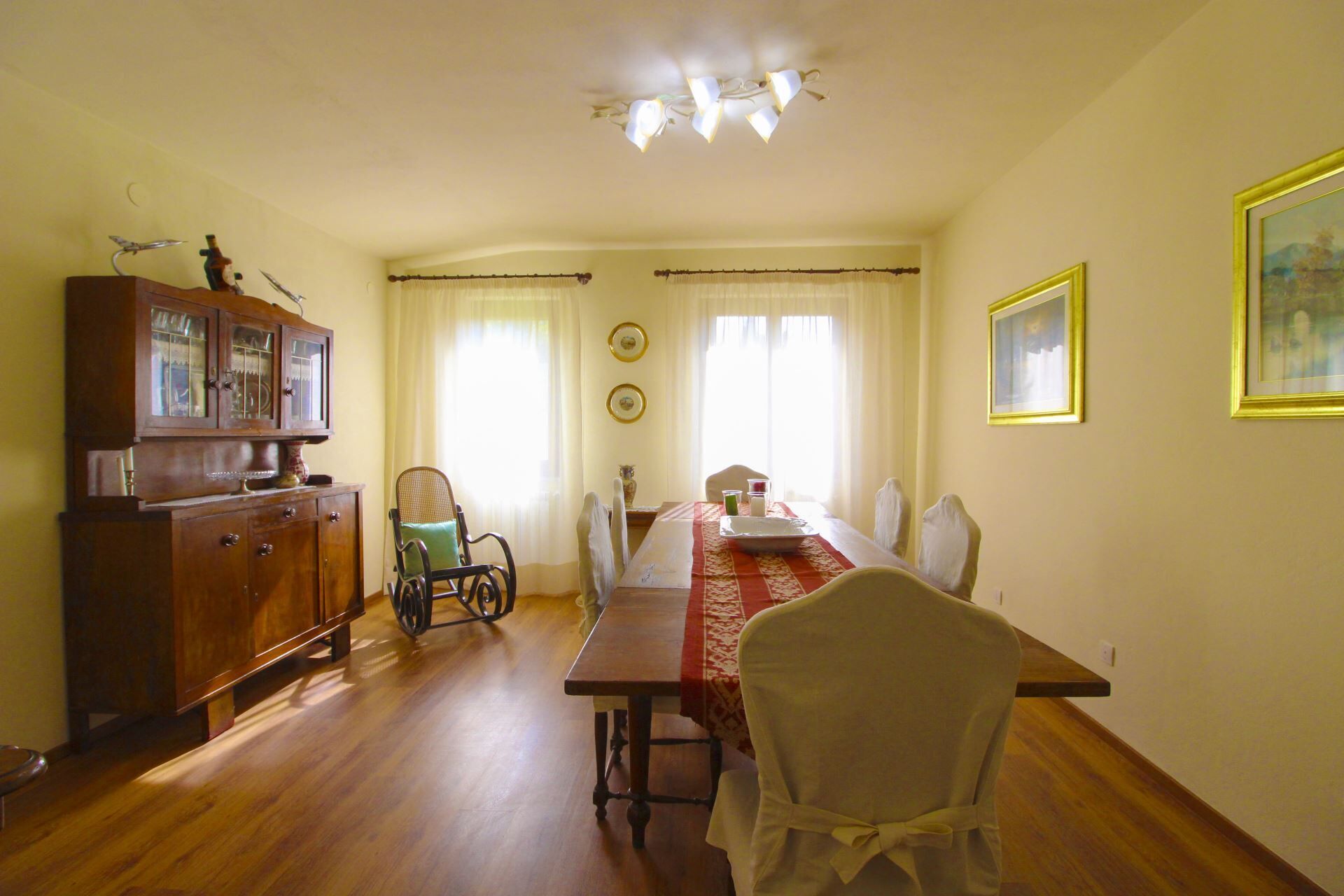A dining room with a wooden table, chairs, a cabinet, and a chandelier.