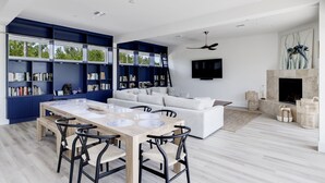 Una sala de estar moderna con comedor, estanterías, un sofá, una chimenea y un televisor montado en la pared.