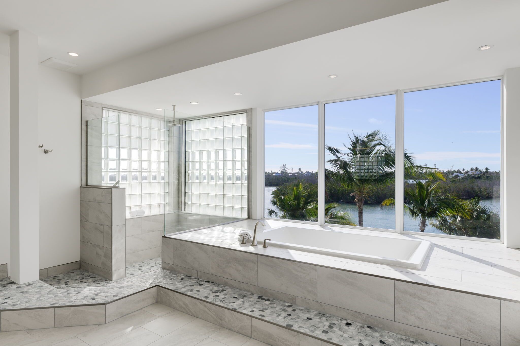 Un baño moderno con una bañera grande, cabina de ducha de vidrio y vistas a una masa de agua.