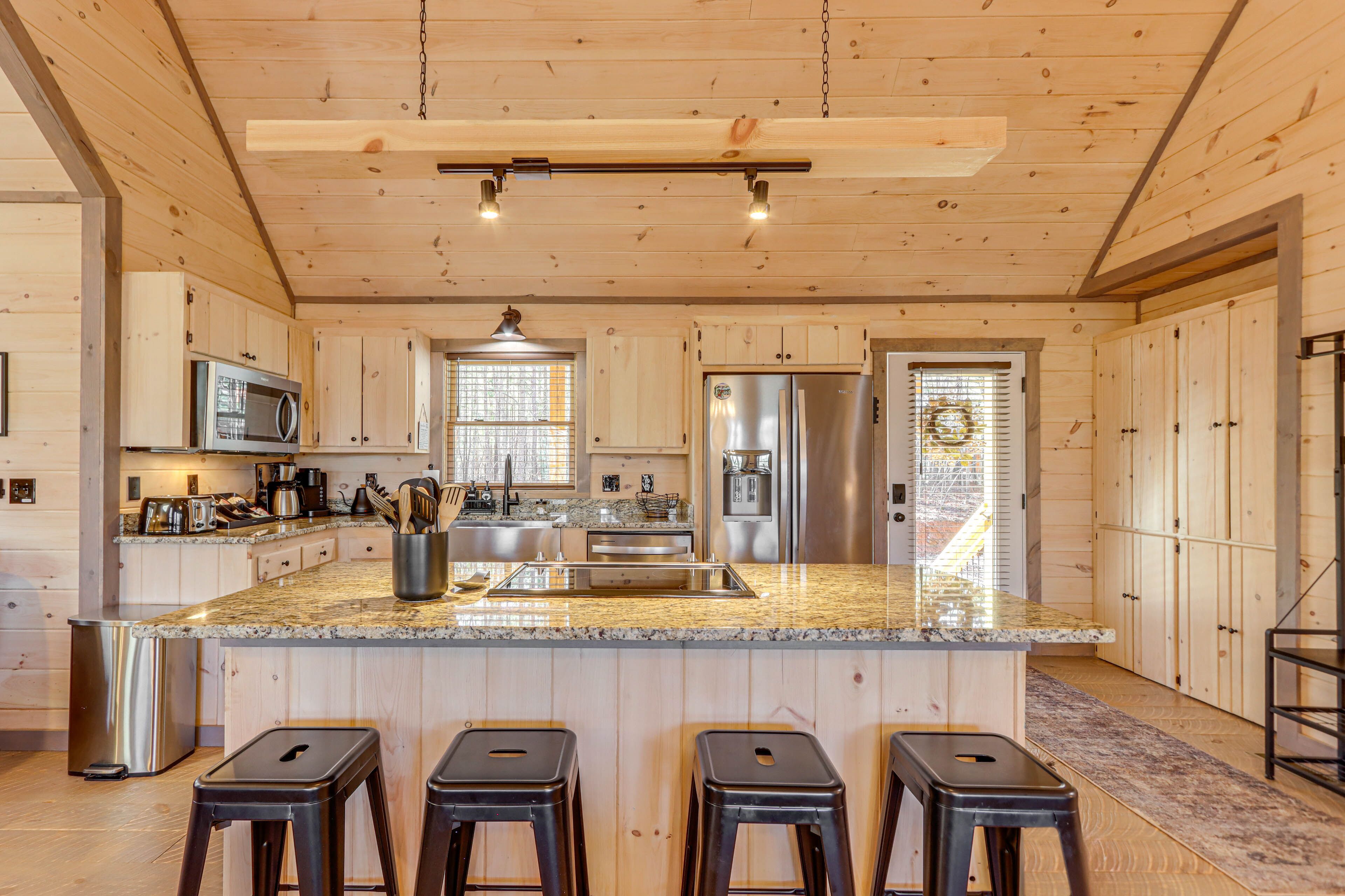 A modern kitchen with wooden cabinets, stainless steel appliances, a granite countertop, and three bar stools.