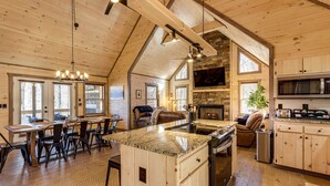 A spacious kitchen with a large island, wooden cabinets, and a stone fireplace. - Cabin w/ Hot Tub & Sauna: 5 Mi to Dtwn Blue Ridge! (Blue Ridge)