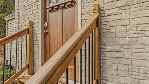 A wooden staircase with a metal railing leading to a stone wall door. - Paws and Pines Retreat! (Ellsworth)