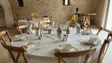 Mesa redonda de comedor con mantel blanco, rodeada de sillas de madera, dispuesta para una comida con velas y flores.