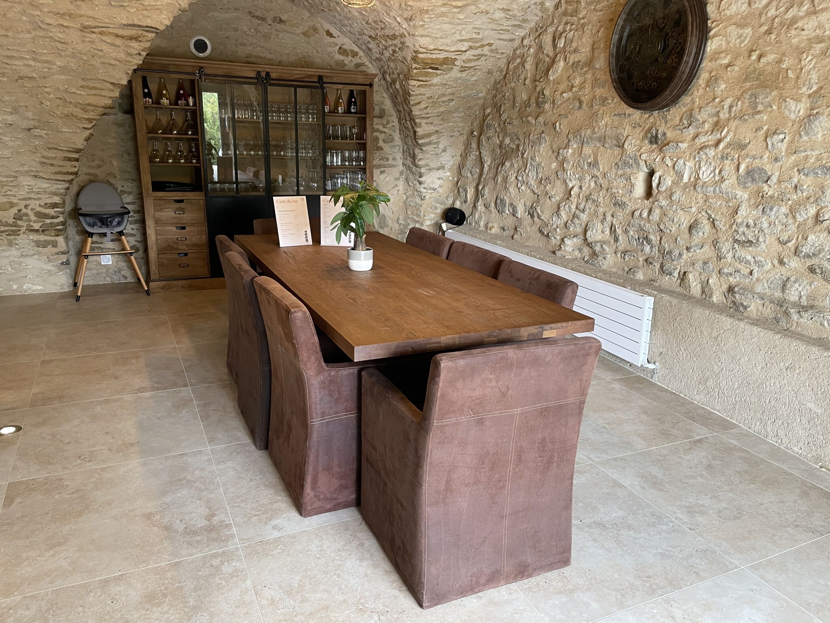 Un comedor rústico con una mesa de madera y asientos tipo banca de cuero, una estantería para vinos con botellas y una pared de piedra.