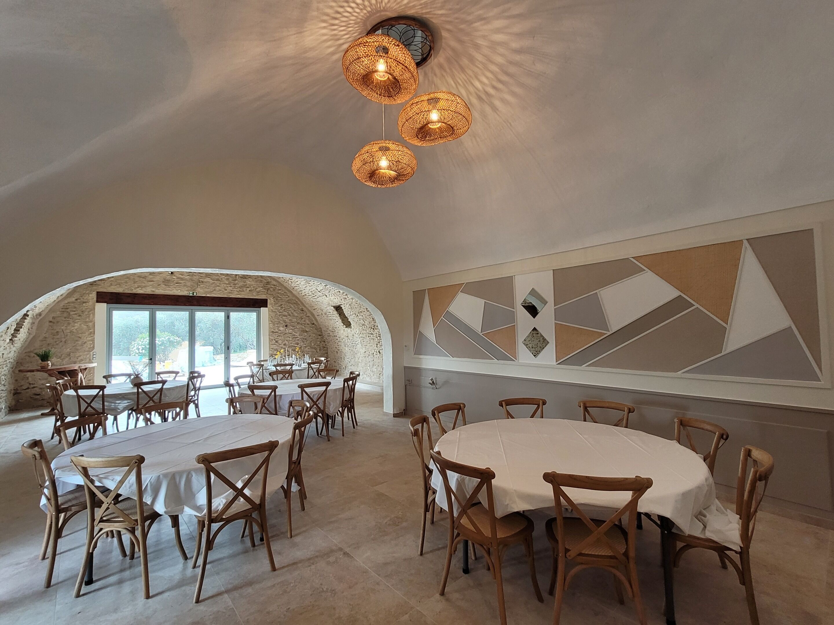 Un vaste espace dédié à la salle à manger, avec des tables rondes et des chaises en bois, agrémenté d’un mur en pierre et d’un motif géométrique sur un autre mur.