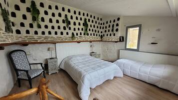 Een slaapkamer met een stenen muur, twee bedden, een stoel en een houten bank.