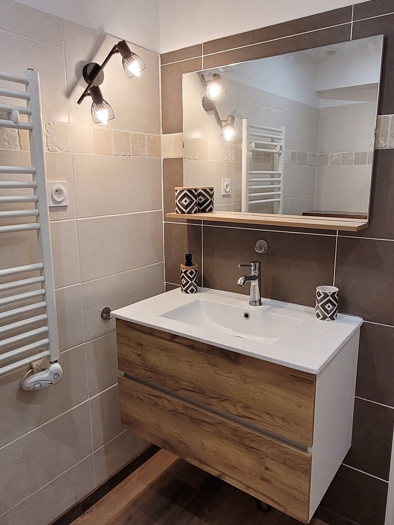 A bathroom with a white sink, wooden vanity, and a large mirror. There is a towel rack and a showerhead on the wall.