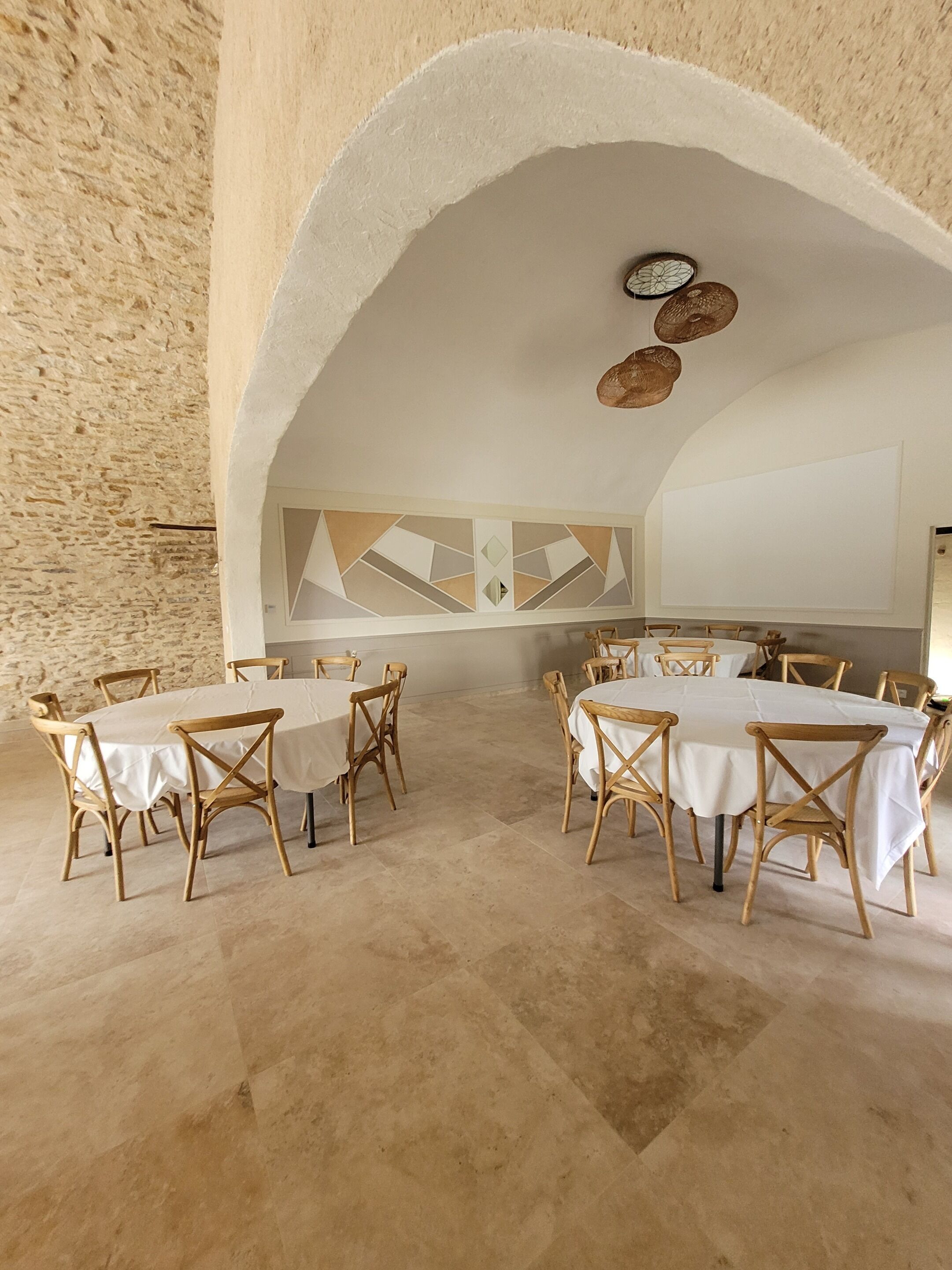 A dining area with round tables and wooden chairs, an arched ceiling, and a stone wall.