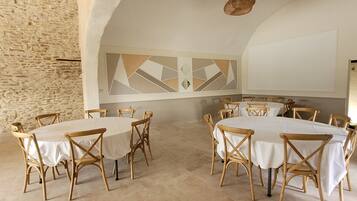 A dining area with round tables and wooden chairs, an arched ceiling, and a stone wall.