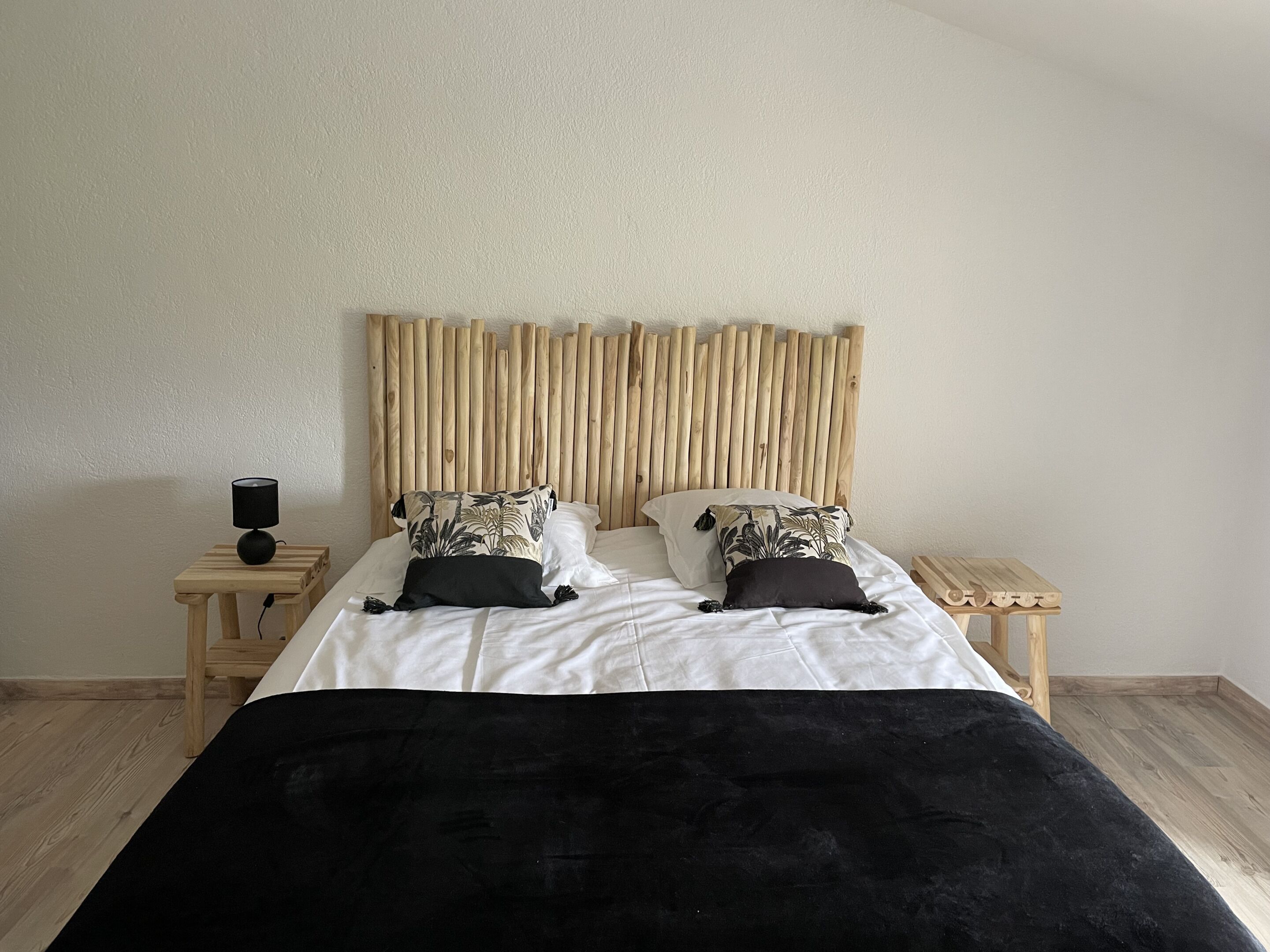 A bed with a wooden headboard, two bedside tables, and a black throw blanket.