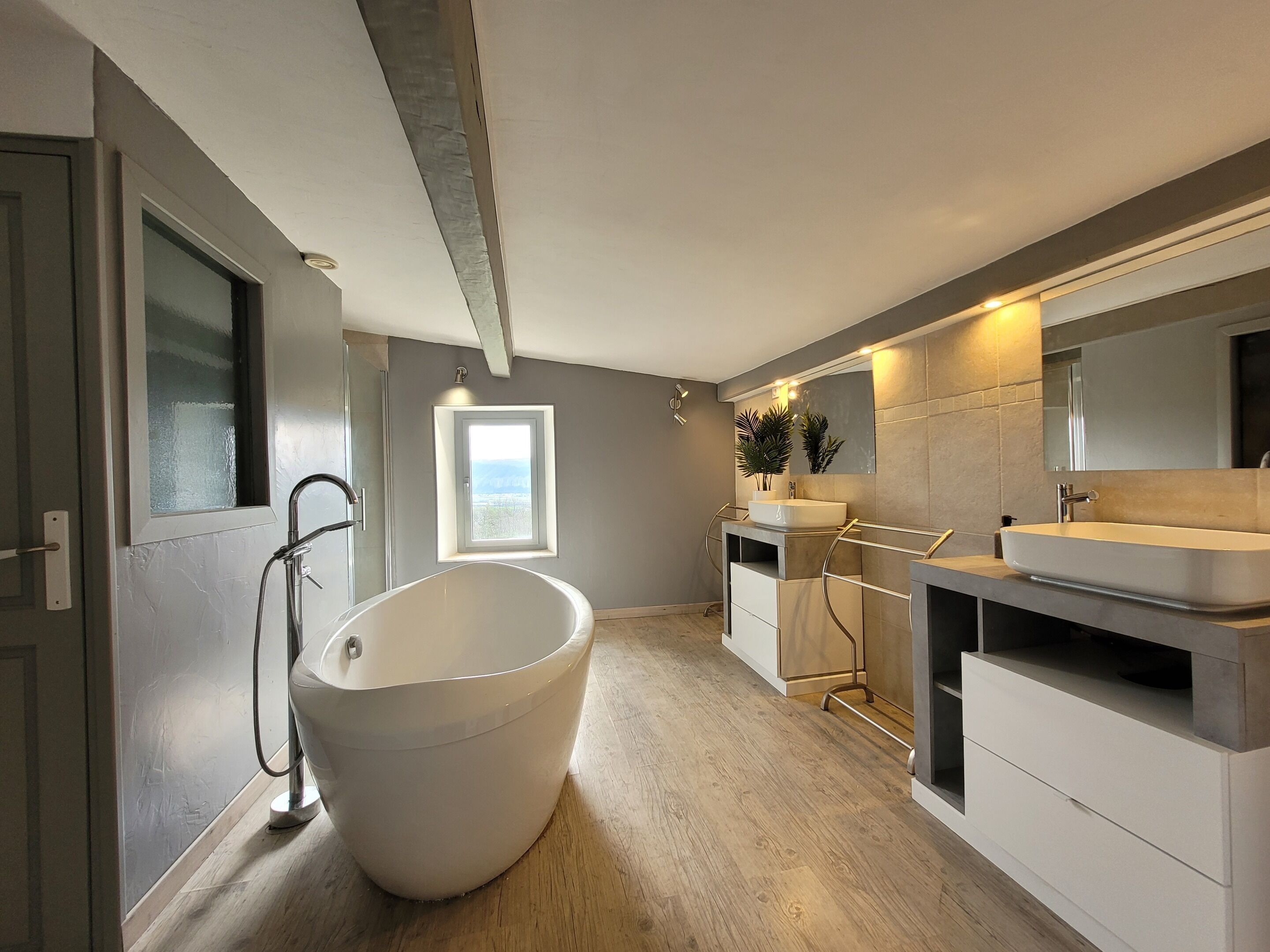 Un baño moderno con una bañera independiente, dos lavamanos y un espejo grande.