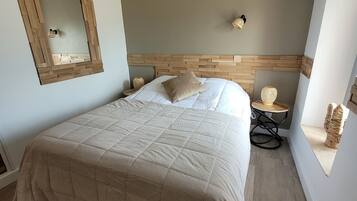 A bedroom with a large bed, wooden headboard, a wall-mounted mirror, and a small table with a lamp.