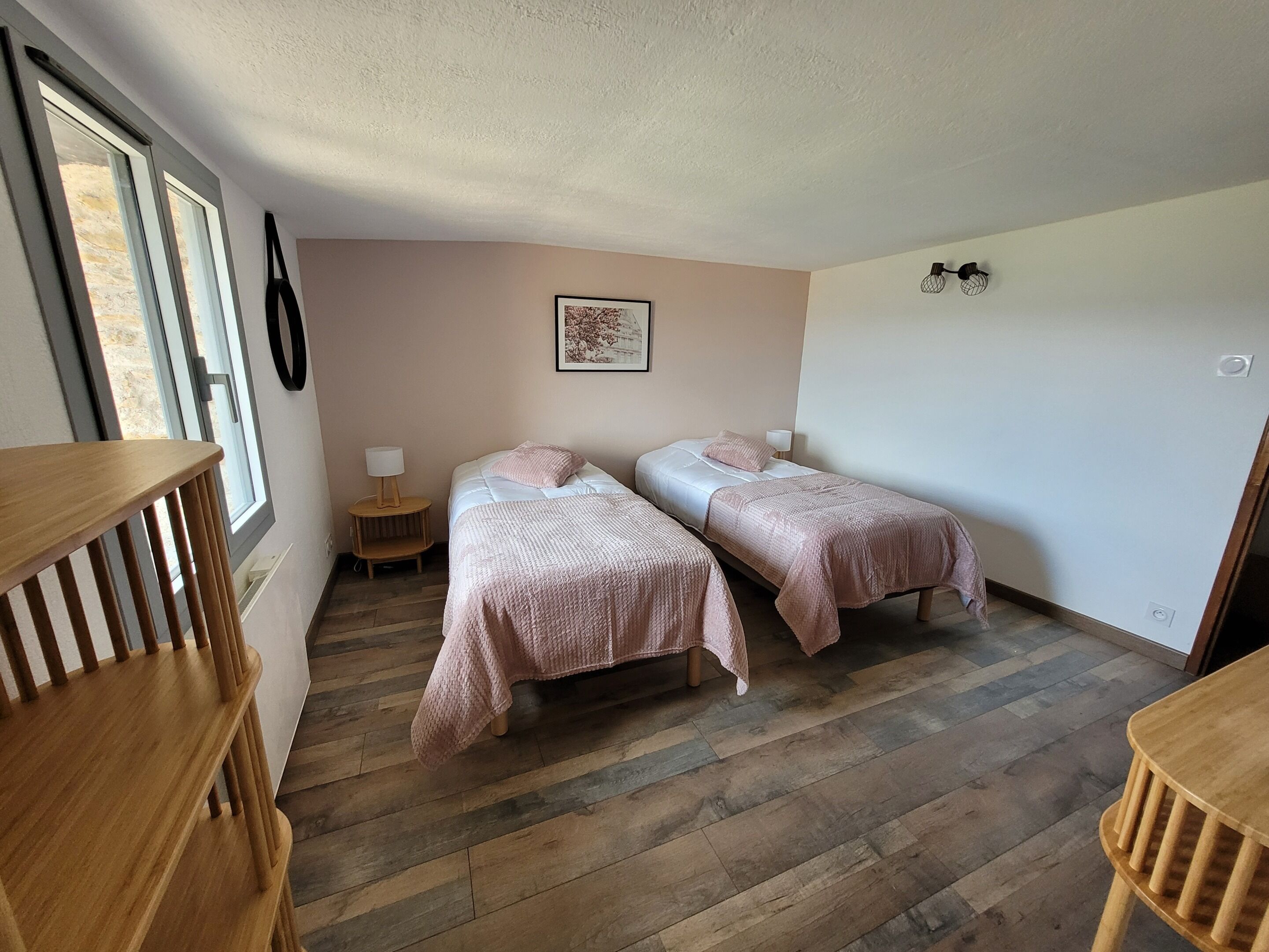 Un dormitorio con dos camas individuales, suelo de madera, una mesita de noche con lámpara y una ventana con persianas.