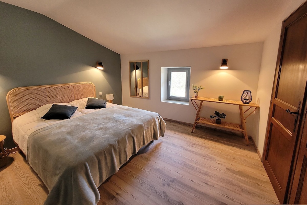 A bedroom with a bed, bedside lamps, a small table with a plant, a window, and a door.
