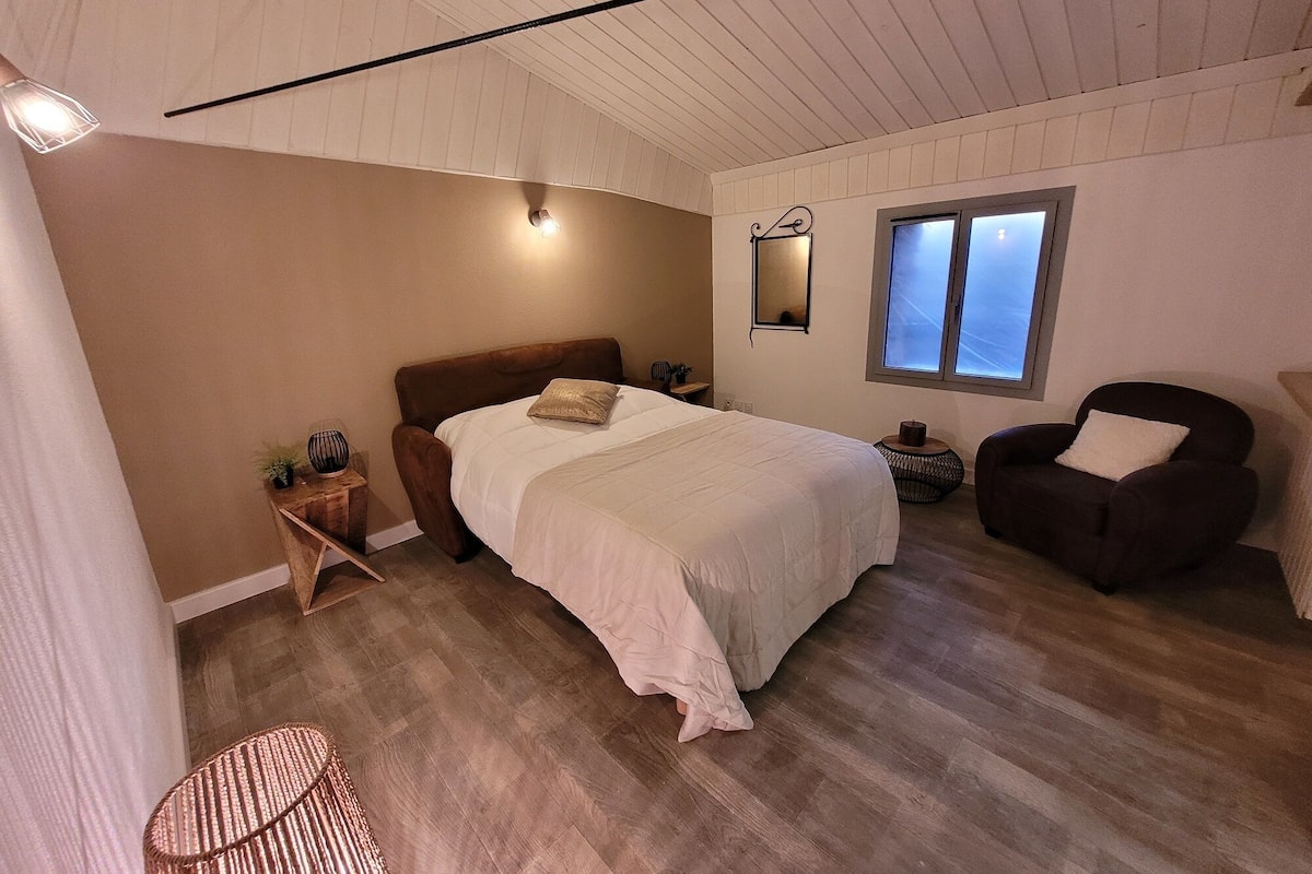 A bedroom with a bed, a chair, a small table, and a window.