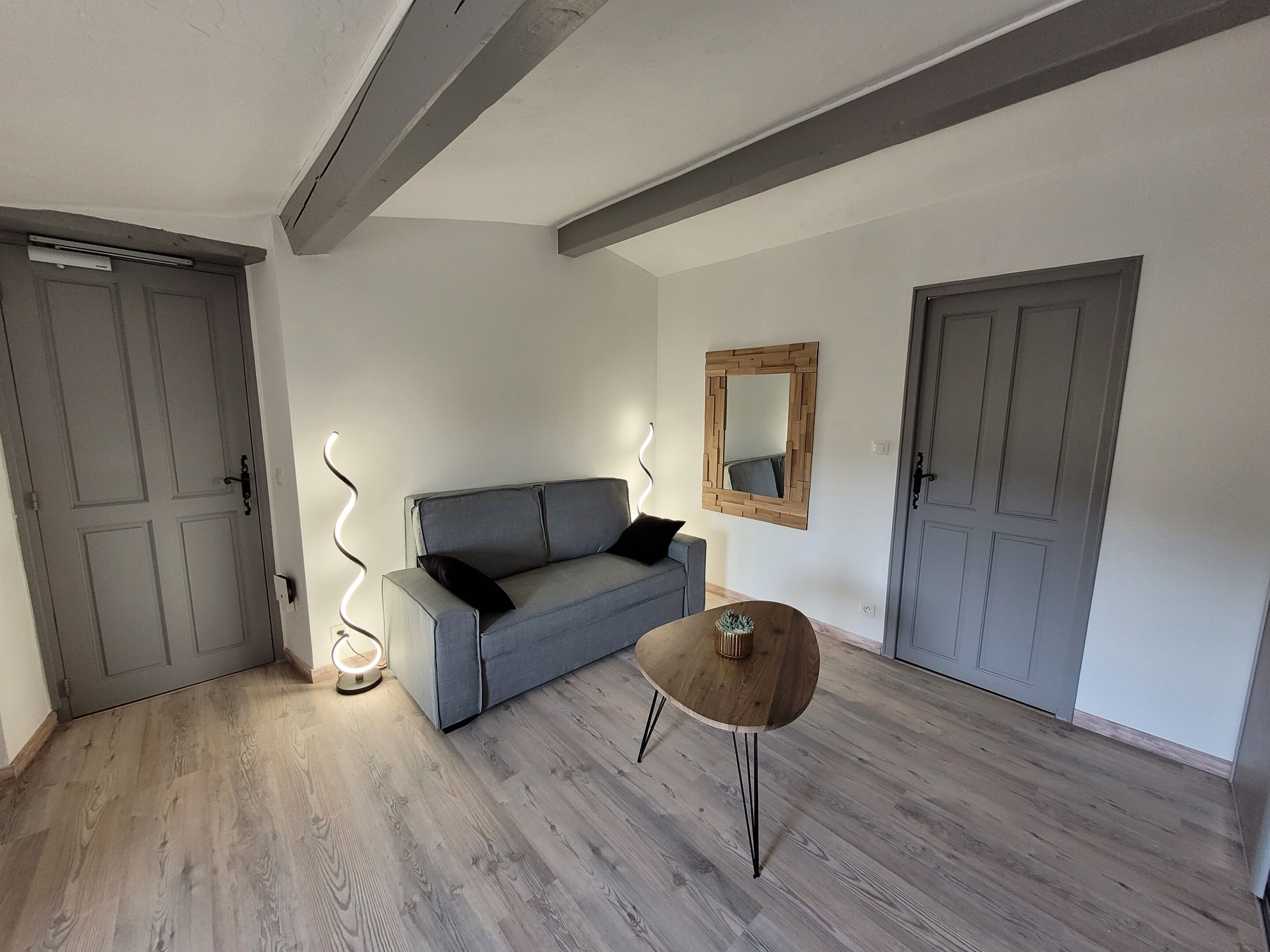 A room with a grey sofa, a small wooden table, and a mirror on the wall.