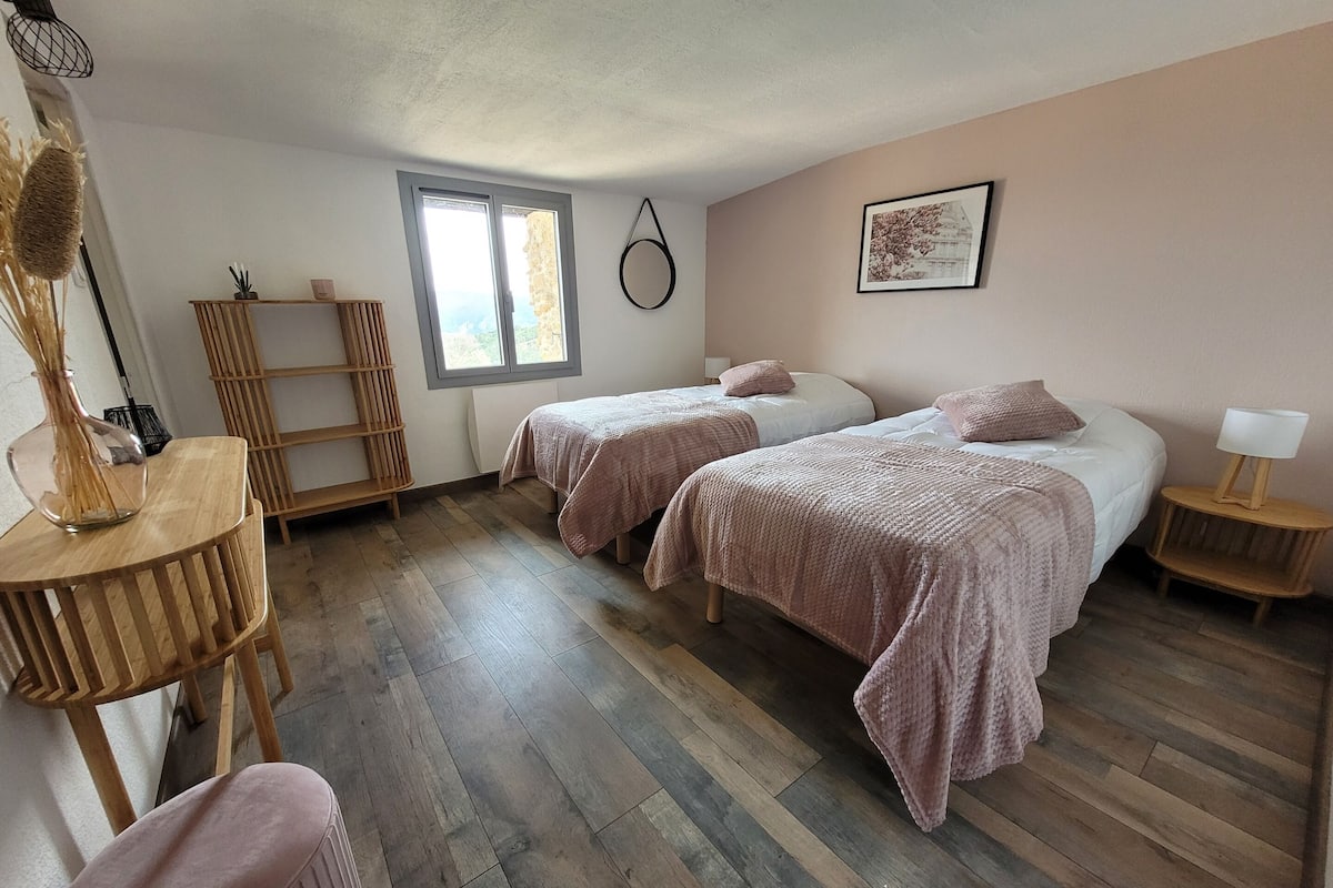 A bedroom with two beds, a window, a wooden floor, a bedside table, and a lamp.
