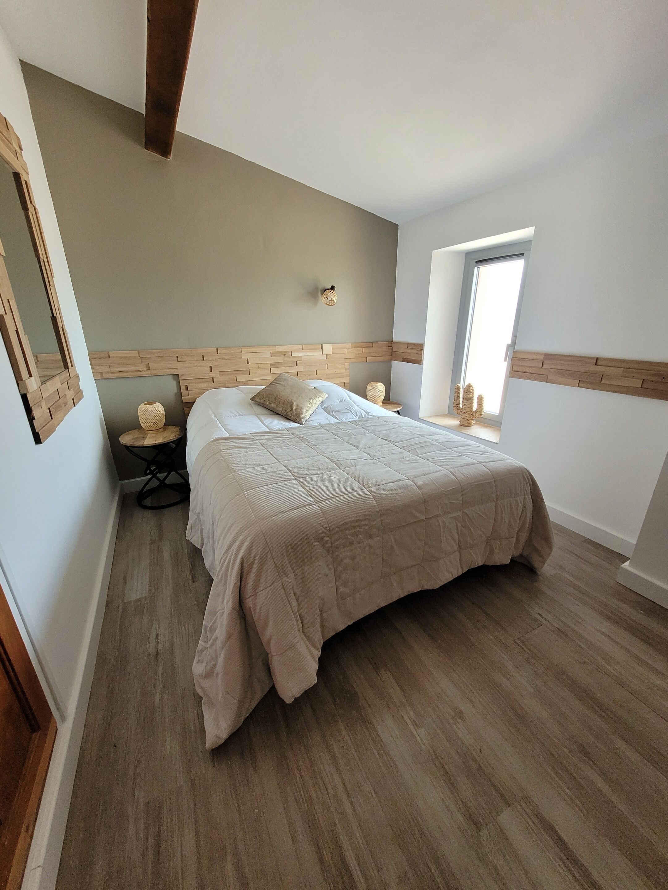 A bedroom with a bed, a small round table, a wall-mounted lamp, and a window.