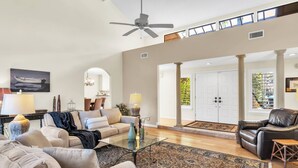 Un salon spacieux avec un plafond haut, un ventilateur de plafond, une grande fenêtre et une vue sur l’extérieur.