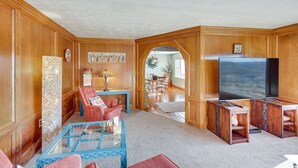 A living room with wooden paneling, a glass coffee table, red armchairs, a TV, and a fireplace. - Charming Farmington Home ~ 16 Mi to Aztec Ruins! (Farmington)