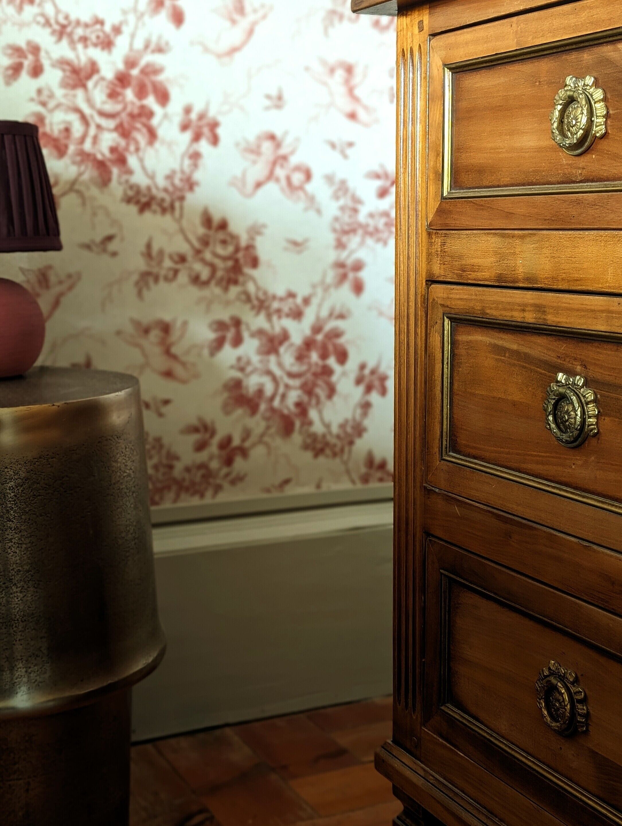 A wooden dresser with ornate handles and a floral wallpaper pattern in the background.