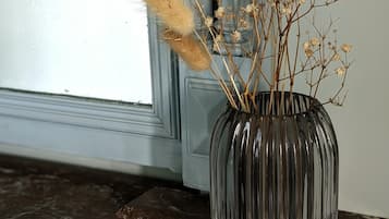 Un jarrón con plantas secas sobre una superficie de mármol oscuro cerca de una ventana.
