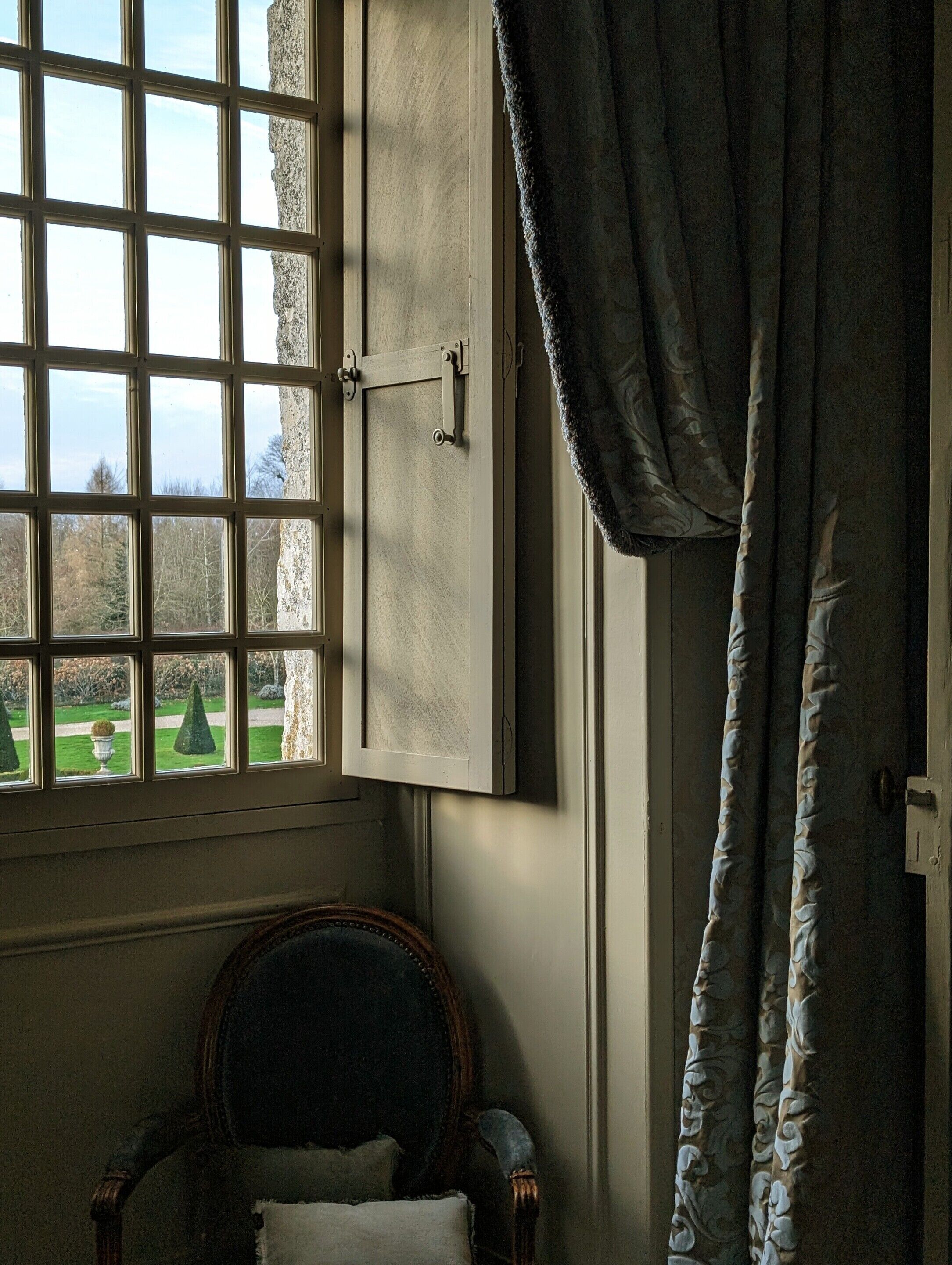 Una habitación con ventana, una silla y una cortina.