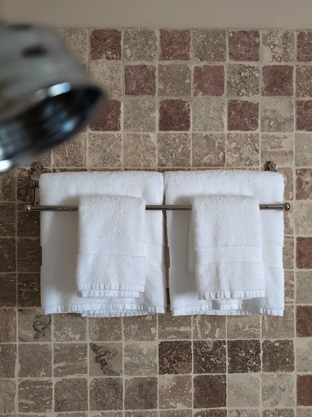 A bathroom with a tiled wall and two white towels hanging on a metal rack.
