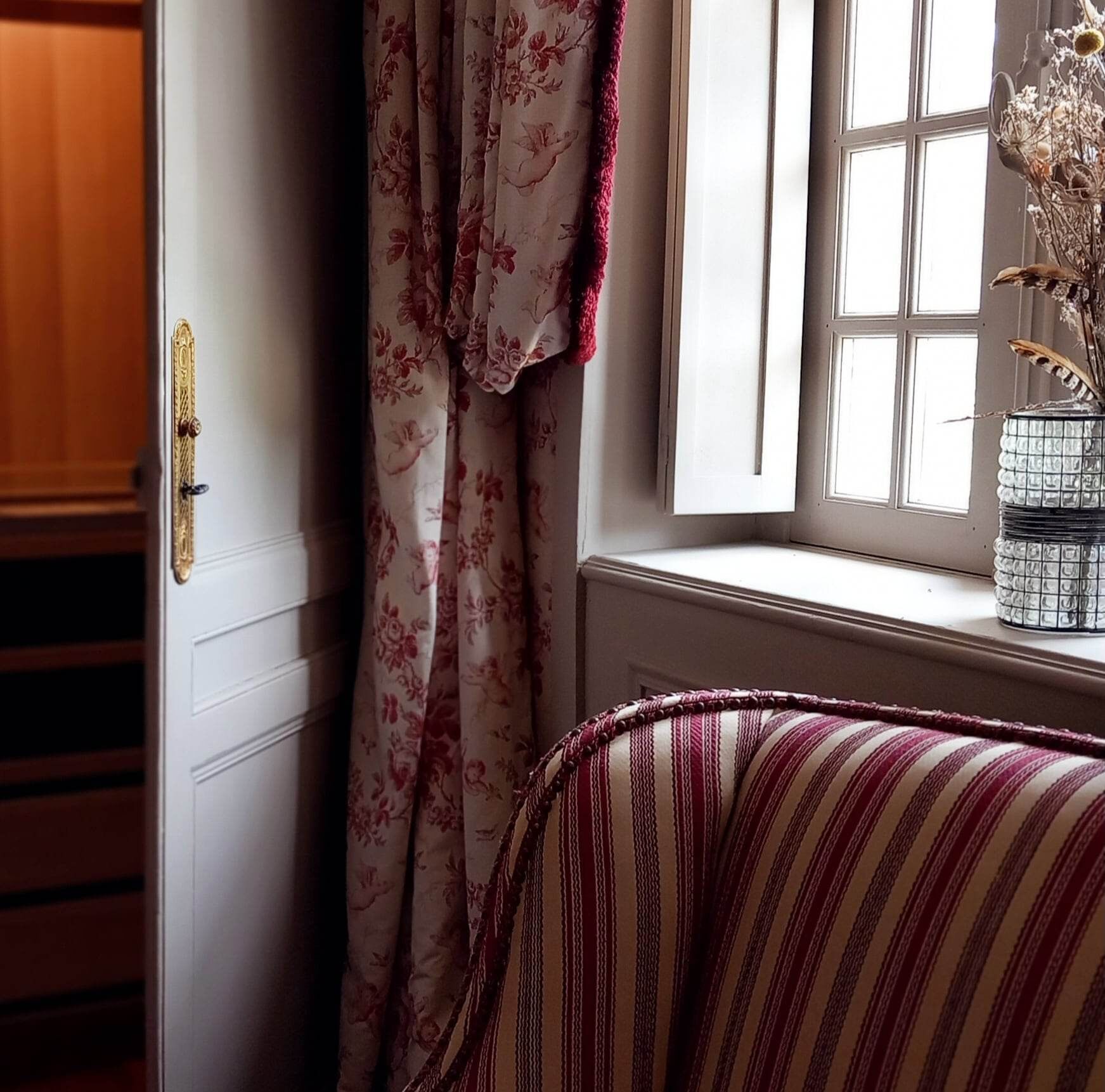 Een kamer met een raam, een deur met een messing knop, en een gestreept kussen op een bed.