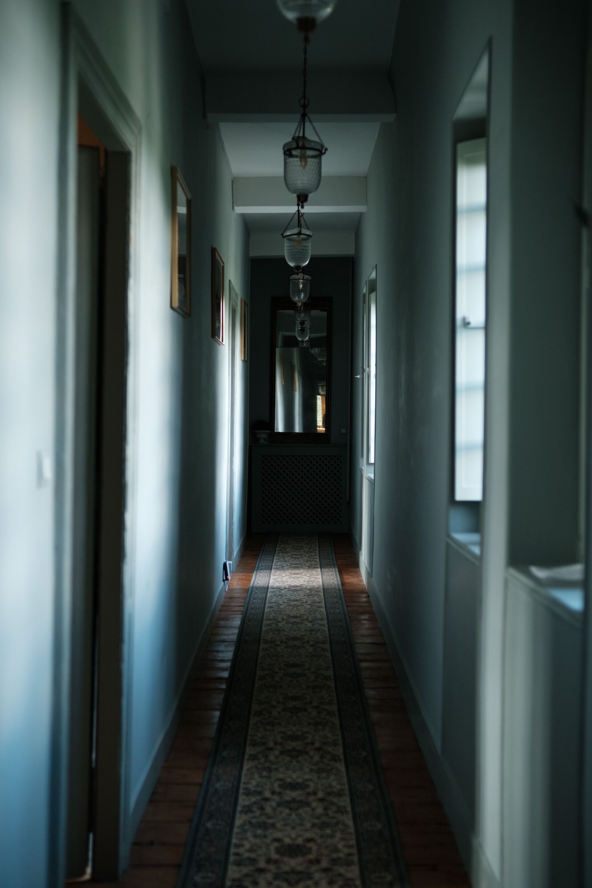 A hallway with a patterned carpet, framed pictures on the walls, and a hanging light fixture.