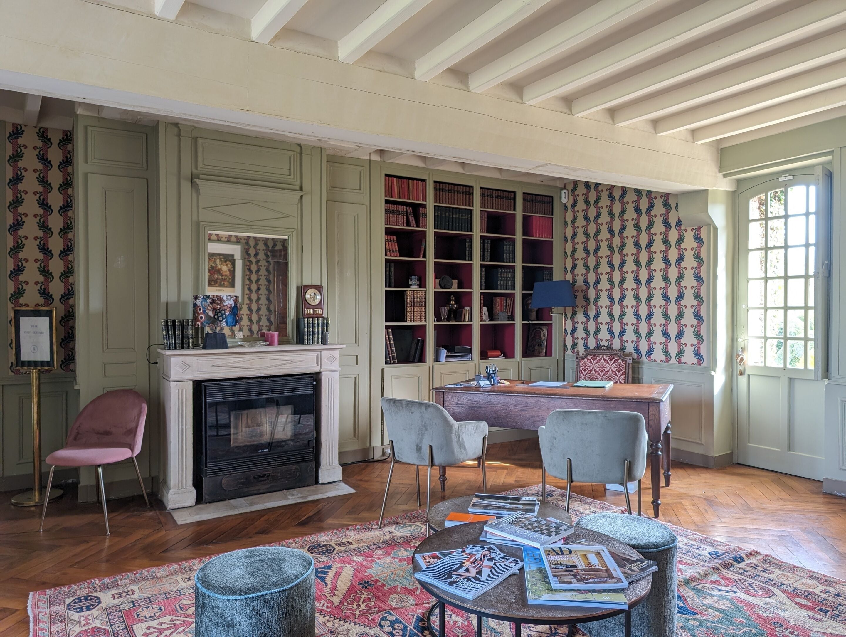 A room with a fireplace, bookshelves, a desk, and a patterned rug.