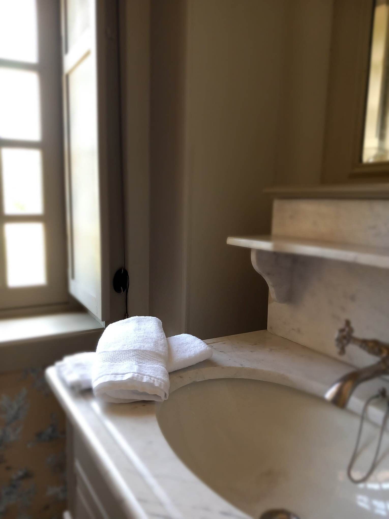 A bathroom with a white sink, a towel on the counter, and a window with blinds.