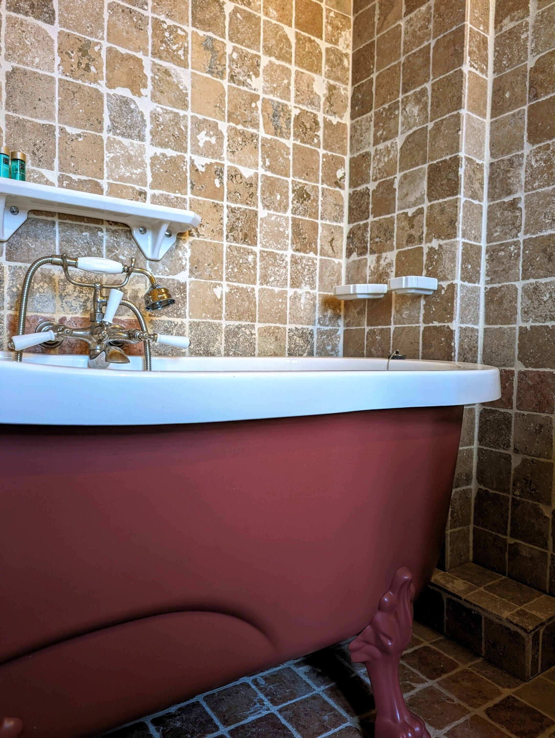 Una bañera de patas de león antigua con un lavabo blanco, frente a una pared revestida con azulejos formando un diseño de ladrillo.