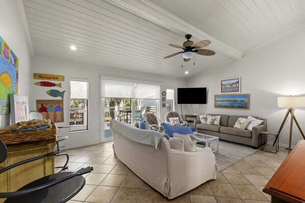 A spacious living room with a ceiling fan, a large sofa, a television, and a dining area with a table and chairs.