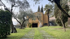 A building with a stone pathway leading to a dark entrance, surrounded by trees and grass. - Villa Olivella in Sale Marasino (Sale Marasino)