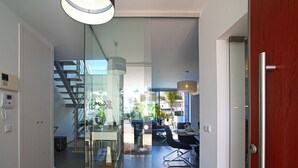 Een modern interieur met een glazen scheidingswand, een trap en een eetgedeelte met uitzicht op het groen.