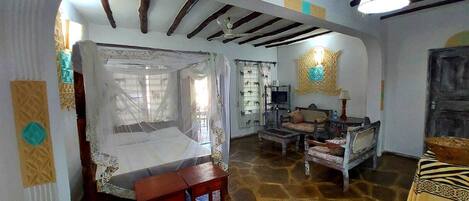 Una habitación con suelo de piedra, una cama con dosel, un banco de madera, un televisor y un adorno en la pared.