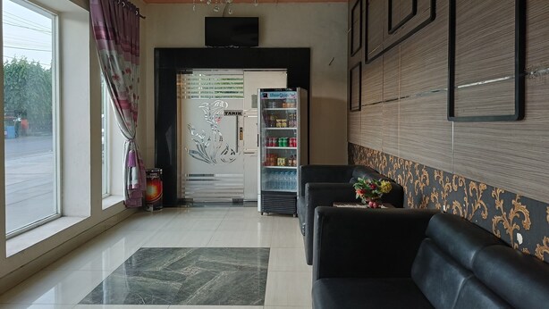 Un'accogliente hall d'albergo con reception, un frigorifero fornito di bevande, una comoda poltrona e un'ampia finestra con tende.