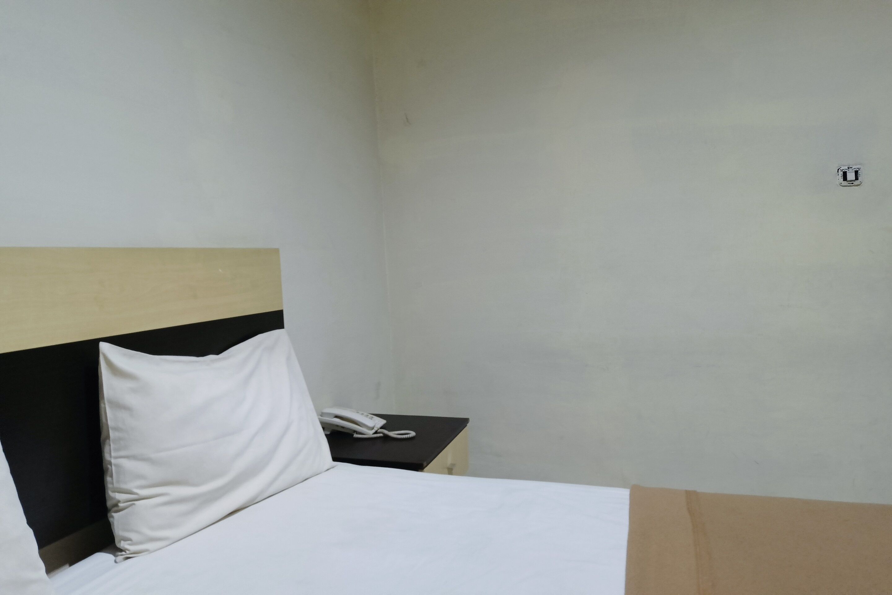Quarto de hotel com uma cama, mesa de cabeceira e telefone.