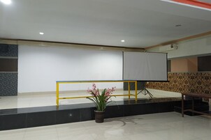 Uma sala de conferências com uma tela branca, um corrimão amarelo e um vaso com planta.