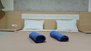 Una camera d'albergo con una testiera in legno, due cuscini bianchi e due asciugamani blu arrotolati sul letto.