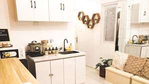 A modern kitchen with white cabinets, a black sink, and a stove. There is a small dining area with a wooden table and a beige sofa. - Studio bedroom in Circulo Verde near Eastwood Quezon city. Pet-Friendly! (Quezon City)