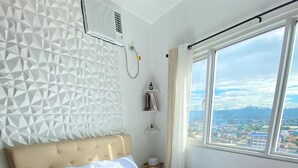 A bedroom with a geometric-patterned wall, a bed with white linens, a beige headboard, and a view of a cityscape through a large window. - Studio bedroom in Circulo Verde near Eastwood Quezon city. Pet-Friendly! (Quezon City)