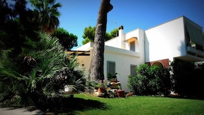 A modern two-story house with a white exterior, a visible chimney, and a well-maintained garden with palm trees and potted plants. - Villa Virginia: private pool, walk 3min for beach and 30min for Paestum temples. (Licinella-Torre di Paestum)