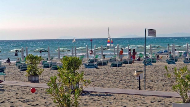 A beach with rows of green and white striped beach chairs and umbrellas, a sailboat in the water, and a sign in Italian. - Villa Virginia: private pool, walk 3min for beach and 30min for Paestum temples. (Licinella-Torre di Paestum)