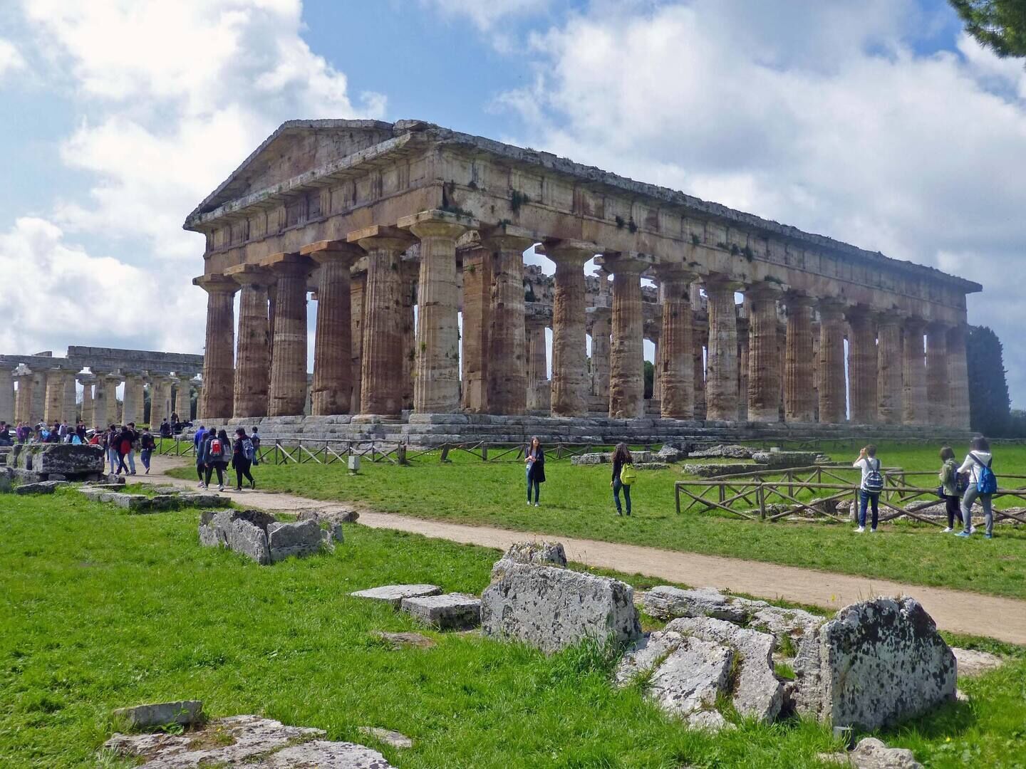 A large ancient Greek temple with columns and visitors around it.