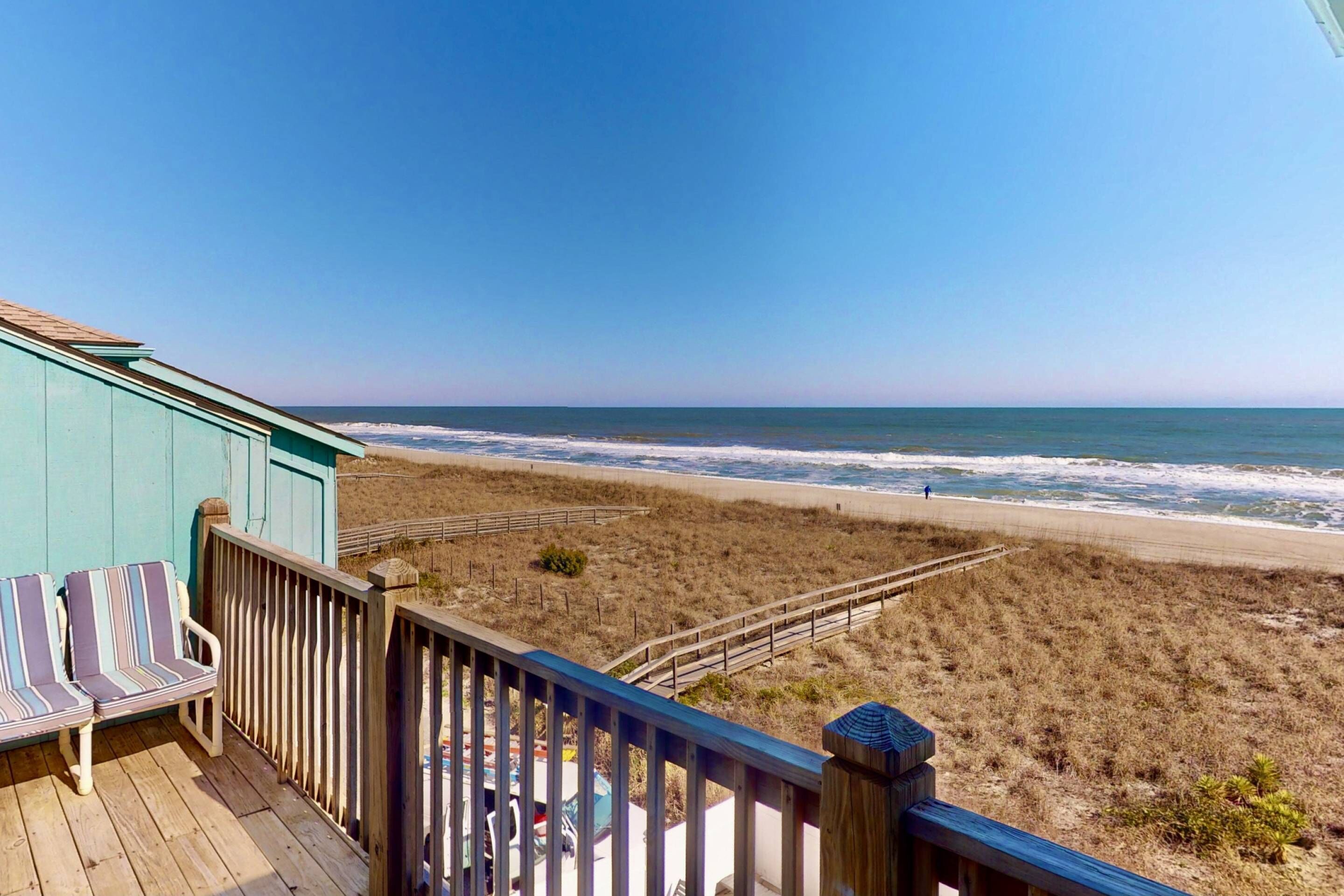 A beach view from a wooden deck with striped chairs and a railing.