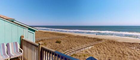 A beach view from a wooden deck with striped chairs and a railing.