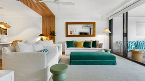 A modern living room with a white sofa, a green ottoman, and a wooden slatted ceiling.