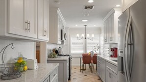 Una cocina moderna con armarios blancos, electrodomésticos de acero inoxidable, una encimera de mármol y un comedor con mesa y sillas.